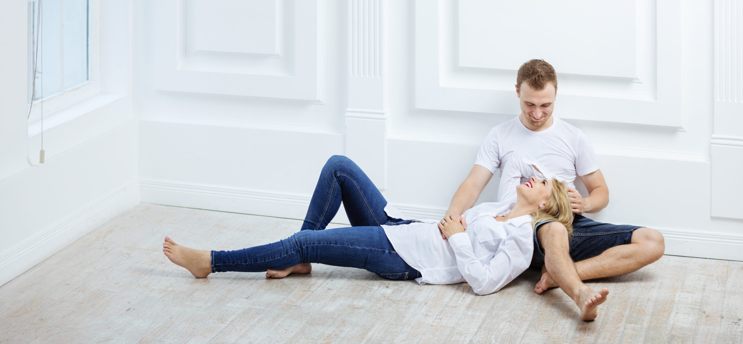 Young couple in casual clothes sitting on floor and talking indoors